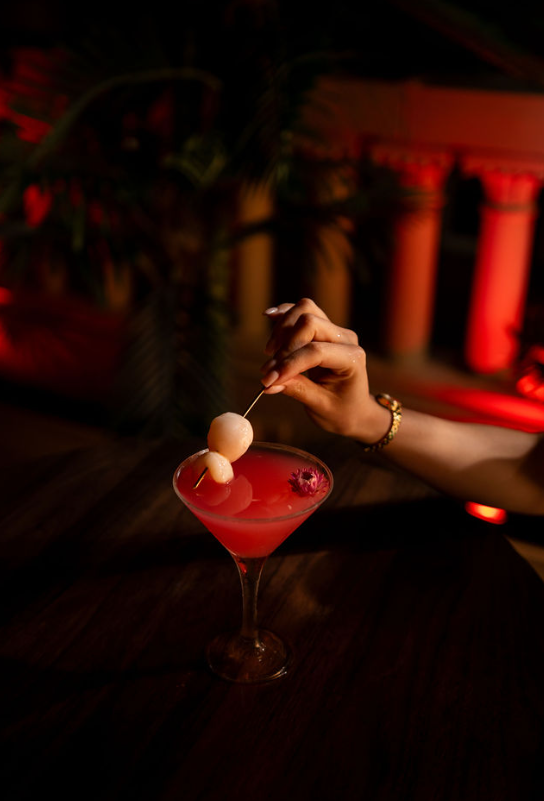 Lychee martini garnished by hand under red lighting