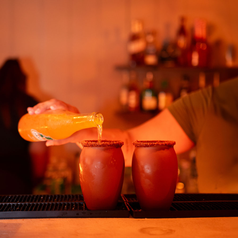 Bartender pouring a micheladas-style drink at the bar